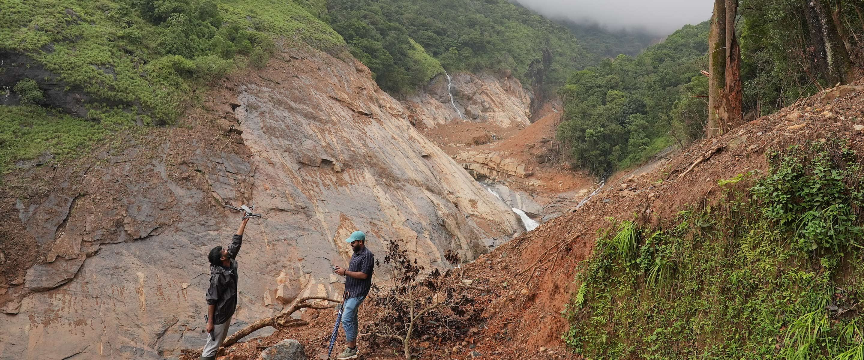 Amrita researchers launching a survey drone beside a landslide-scoured rock face and debris channel